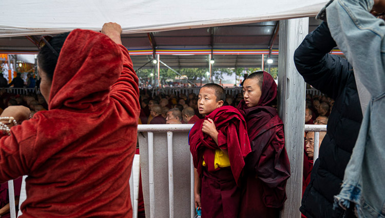 Young monks finding protection from the rain during as His Holiness the Dalai Lama addresses the crowd before conducting an Avalokiteshvara Empowerment at the Kalachakra Ground in Bodhgaya, Bihar, India on January 3, 2020. Photo by Tenzin Choejor