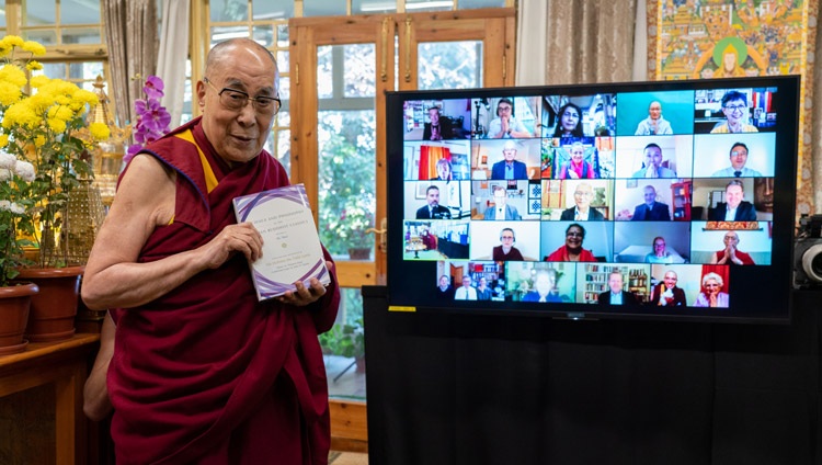 Su Santidad sostiene un ejemplar de «Ciencia y Filosofía en los Clásicos Budistas Indios, Vol. 2 - La Mente» mientras posa en pie frente a la pantalla que muestra los rostros de los diversos colaboradores en su residencia en Dharamsala, HP, India, el 13 de noviembre de 2020. Foto de Ven Tenzin Jamphel