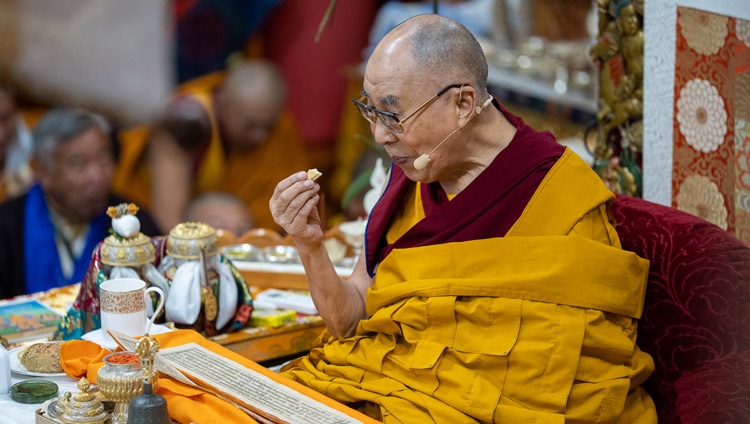 His Holiness the Dalai Lama taking a quick break in the preliminary practices for the Avalokiteshvara Empowerment to enjoy some bread on the second day of his Teachings for Tibetan Youth at the Main Tibetan Temple in Dharamsala, HP, India on June 2, 2022. Photo by Tenzin Choejor