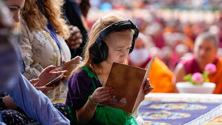 A young girl listening to a live interpretation and following the text "Thirty-seven Practices of All Bodhisattvas" on the first day of teachings at the Shewatsel Teaching Area in Leh, Ladakh UT, India on July 21, 2023. Photo by Ven Zamling Norbu
