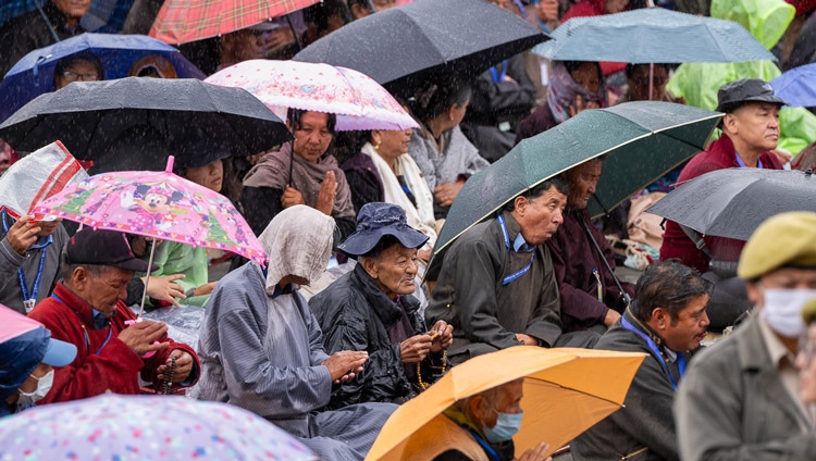 Miembros de la multitud, muchos protegiéndose de la lluvia, escuchando a Su Santidad el Dalái Lama mientras confiere la iniciación de Avalokiteshvara en el terreno de enseñanzas de Shewatsel en Leh, Ladakh, India, el 23 de julio de 2023. Foto de Tenzin Choejor
