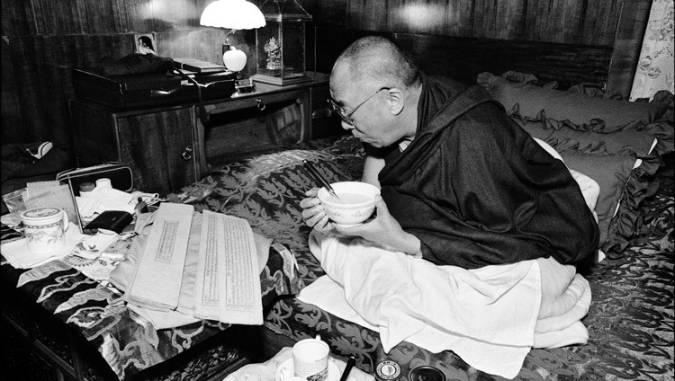 His Holiness the Dalai Lama reading Buddhist texts as he eats breakfast at his residence in Dharamsala, HP, India on 15 August, 2004. (Photo courtesy of Manuel Bauer)